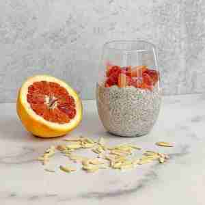 PCOS Breakfast Idea-Blood Orange Chia Pudding inside clear glass next to blood orange sliced in half. Silvered almonds are surrounding glass.