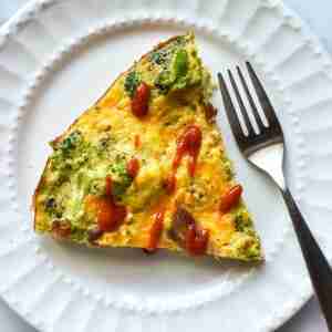 Make ahead PCOS Breakfast Idea-White plate and fork with wedge of Broccoli Bacon Cheddar Frittata with drizzle of hot sauce