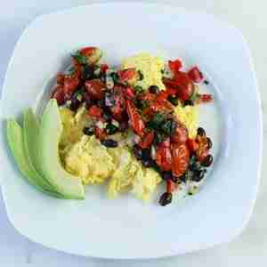 PCOS Breakfast Idea- White plate with scrambled eggs top with black beans, salsa and garnished with avocado.