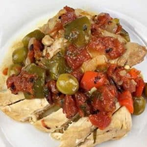 White plate with instant pot chicken stew in the center, containing chicken, red and green bell peppers, tomatoes, onions and olives.