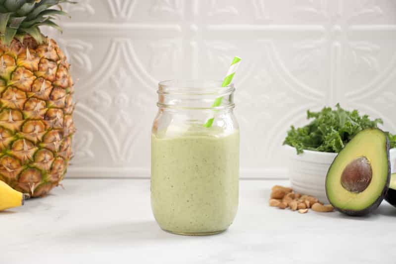 PCOS green smoothie in glass jar with white background including a pineapple, kale, avocado, cashew nuts and banana on display.
