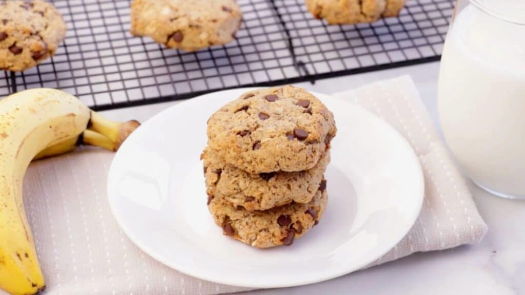 picture of a stack PCOS-friendly oatmeal Chocolate chip breakfast bars on white plate with a banana and glass of milk in background.