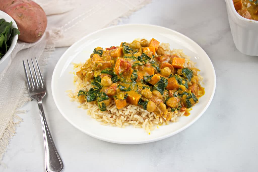 White plate with marble background and fork. Plate filled with a PCOS-friendly curry of chickpea, peanut and spinach over brown rice.