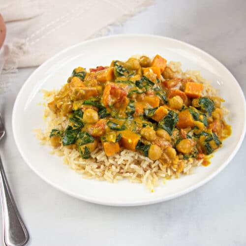 White plate with marble background and fork. Plate filled with a PCOS-friendly curry of chickpea, peanut and spinach over brown rice.
