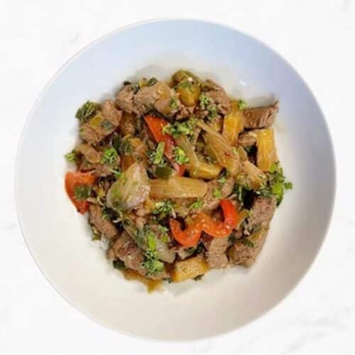 White bowl fill with PCOS-friendly Pineapple Beef stir fry with peppers on white background.